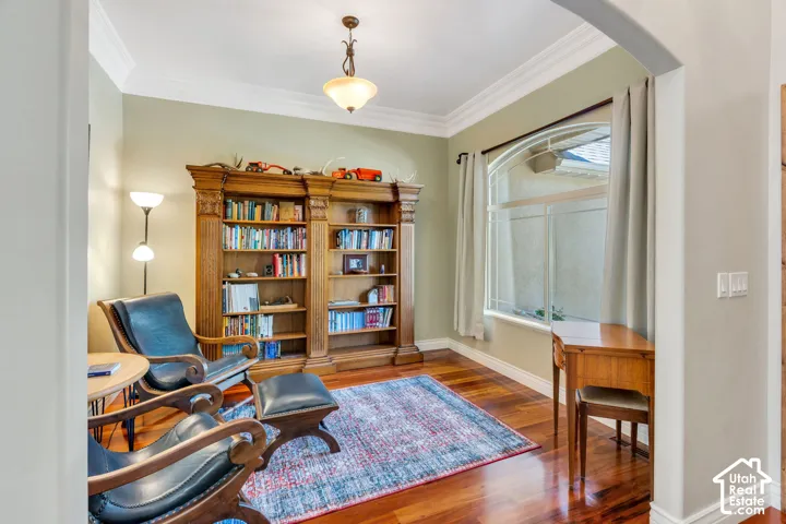 Hardwood flooring, arched window, built-in shelving, crown molding, and a ceiling-mounted light fixture