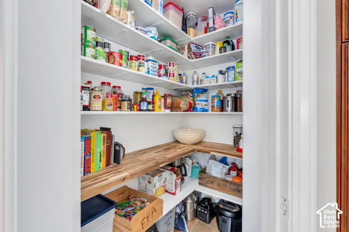 Spacious pantry featuring white shelving, wood-finish corner shelving, and tile flooring