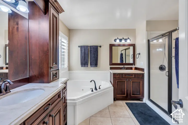 Dual sink vanity with stone-finish countertop, corner soaking tub, separate enclosed shower with dark-framed glass door, and tile flooring