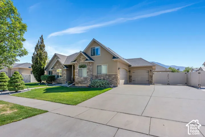 Front exterior featuring stone and stucco finishes, an attached two-car garage, a wide concrete driveway, and a fenced side yard