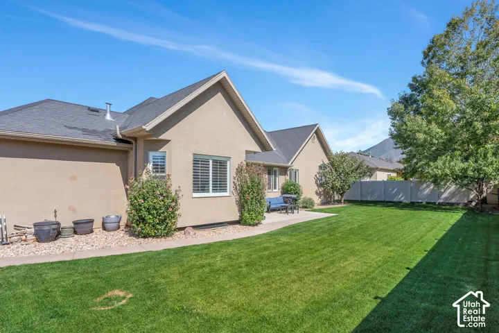 Expansive lawn area with a concrete patio, stucco exterior, and gable roofline
