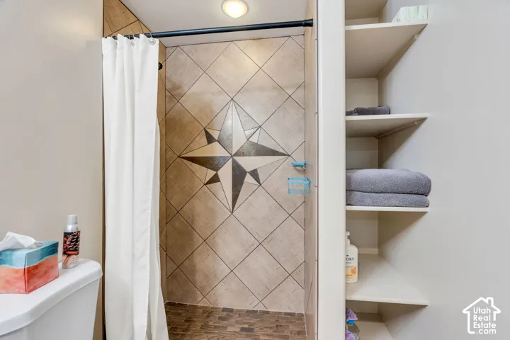 Tile shower with compass rose inlay, dark shower rod, built-in recessed shelving, and a toilet