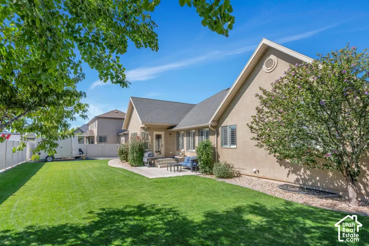 Expansive grassy yard with a concrete patio and stucco exterior, featuring established landscaping and a white privacy fence