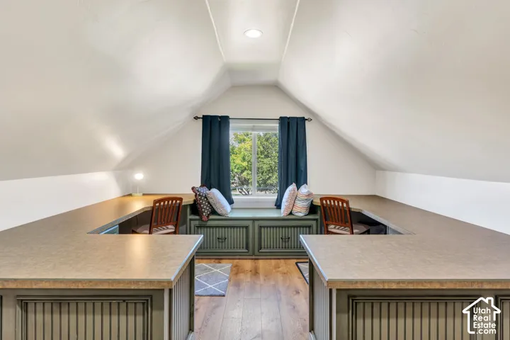 Sloped ceilings, window with natural light, wood-finish flooring, built-in window seating, and built-in desk surfaces