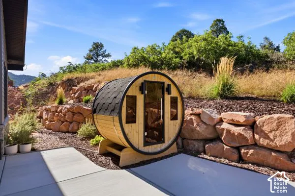 Barrel-style sauna with shingle roof, concrete patio, and stone retaining walls. The photos are renderings only - these photos are for a similar unit in Discovery Ridge. Not this actual model.