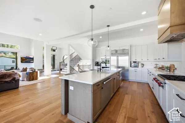 Spacious open-concept interior featuring light wood-finish flooring, a modern kitchen island with pendant lighting, white cabinetry, integrated stainless steel appliances, and a large window. The photos are renderings only - these photos are for a similar