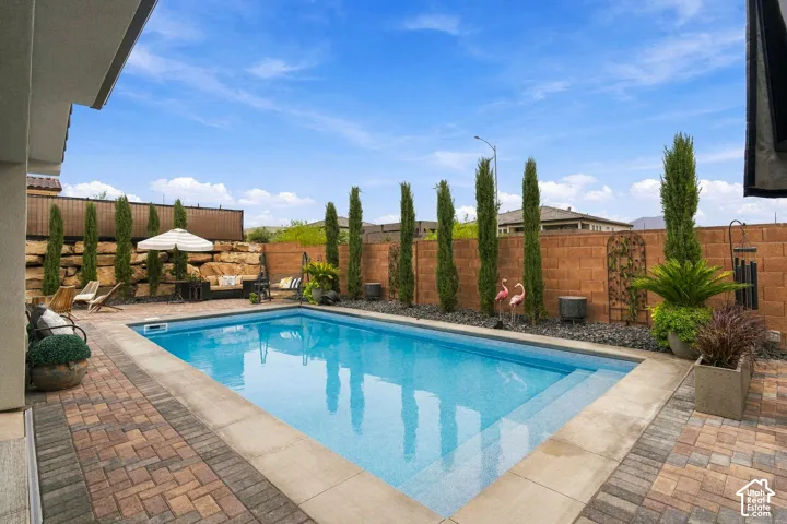 Outdoor swimming pool with integrated steps, surrounded by paver patio, natural rock retaining wall, and mature columnar evergreens