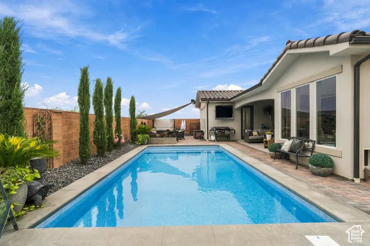 Outdoor swimming pool with concrete surround, brick privacy wall, and mature columnar trees
