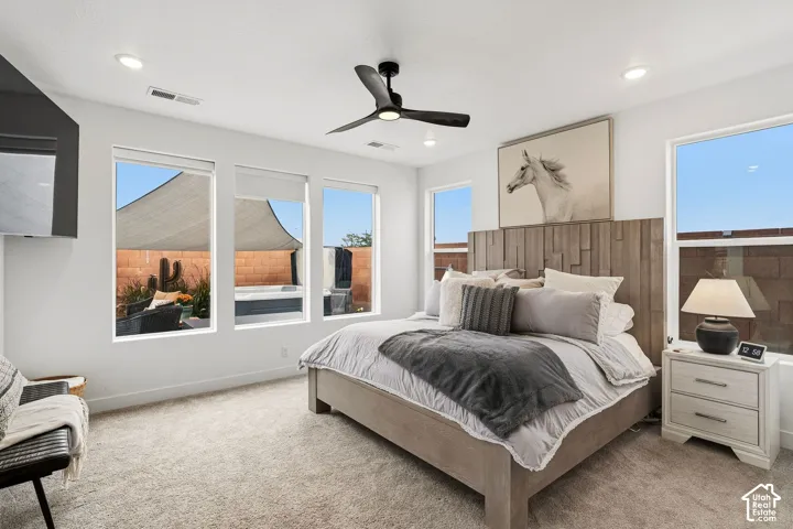 Recessed lighting with a ceiling fan, multiple windows with roller shades, and a textured headboard