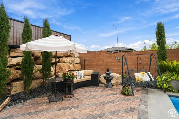 Brick paver patio, natural rock retaining wall, mature columnar evergreens, tiered water feature, and block perimeter fencing