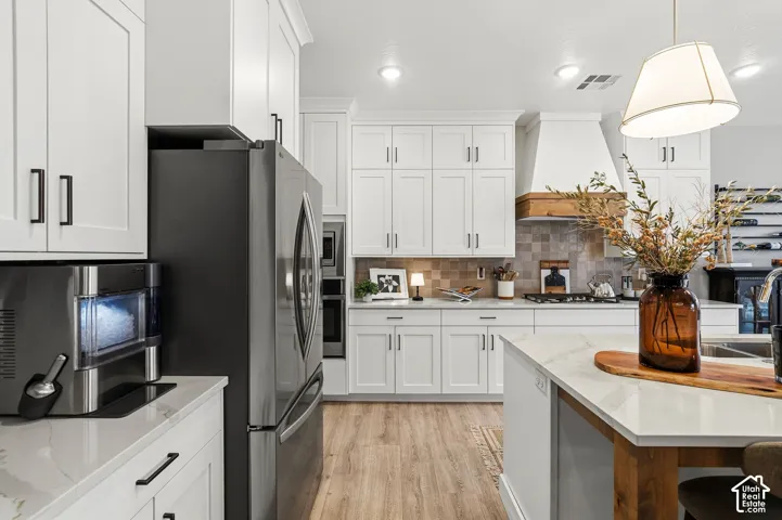 White shaker-style cabinetry with matte black hardware, light-toned wood-finish flooring, a kitchen island with a light-toned countertop, a tile backsplash, and recessed lighting