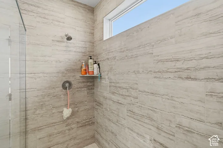 Walk-in shower with full-height tile surround, fixed showerhead, integrated shelf, and glass panel enclosure