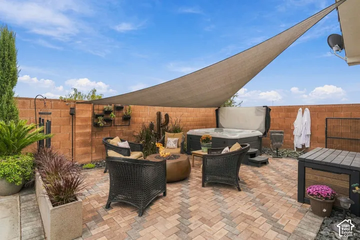 Paver patio featuring a hot tub, shade sail, and block wall perimeter