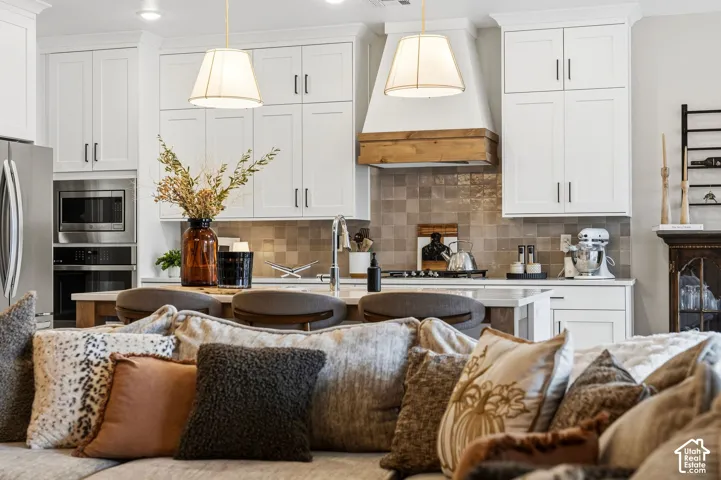 White shaker cabinetry, stainless steel appliances, tile backsplash, built-in oven and microwave, and a wooden range hood