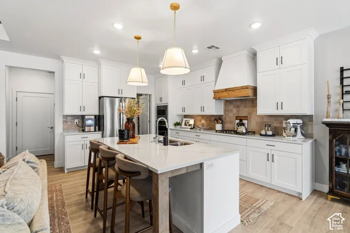 White shaker-style cabinetry, a spacious kitchen island with seating, stainless steel appliances, a wood-finish range hood, and wood-finish flooring
