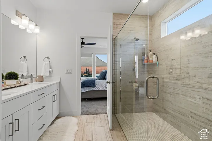 Spacious bathroom featuring a dual vanity with white cabinetry, a large frameless glass shower, a transom window, and wood-finish flooring