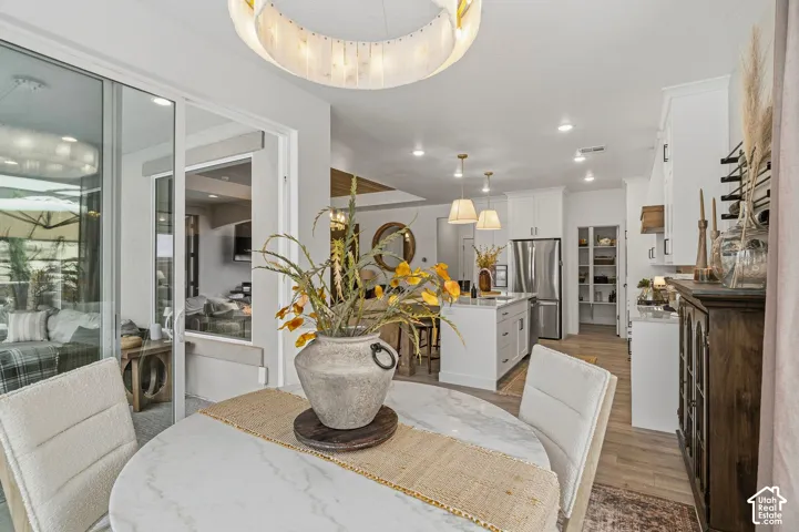 Open-concept dining area with a circular, light-colored tabletop, adjacent to a kitchen featuring white cabinetry and an island with pendant lighting
