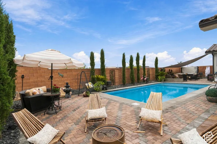 In-ground swimming pool, brick paver patio, block wall perimeter, mature columnar evergreen trees, and a built-in fire pit