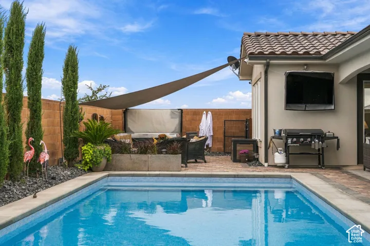 Sparkling swimming pool with surrounding paver patio, integrated shade sail, and exterior-mounted television