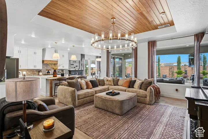 Open-concept living space featuring a wood-panel accent ceiling, a large linear chandelier, and wood-finish flooring