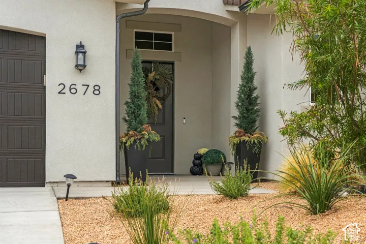 Stucco exterior featuring a covered entryway with a recessed door and transom window, exterior wall lantern, and a concrete pathway with gravel landscaping