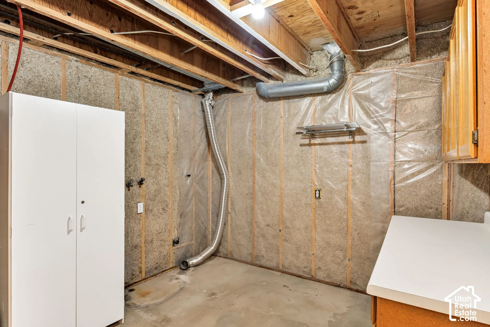 Unfinished basement area with exposed wood joists and subflooring, unfinished walls with insulation and vapor barrier, concrete flooring, and an exposed ventilation duct
