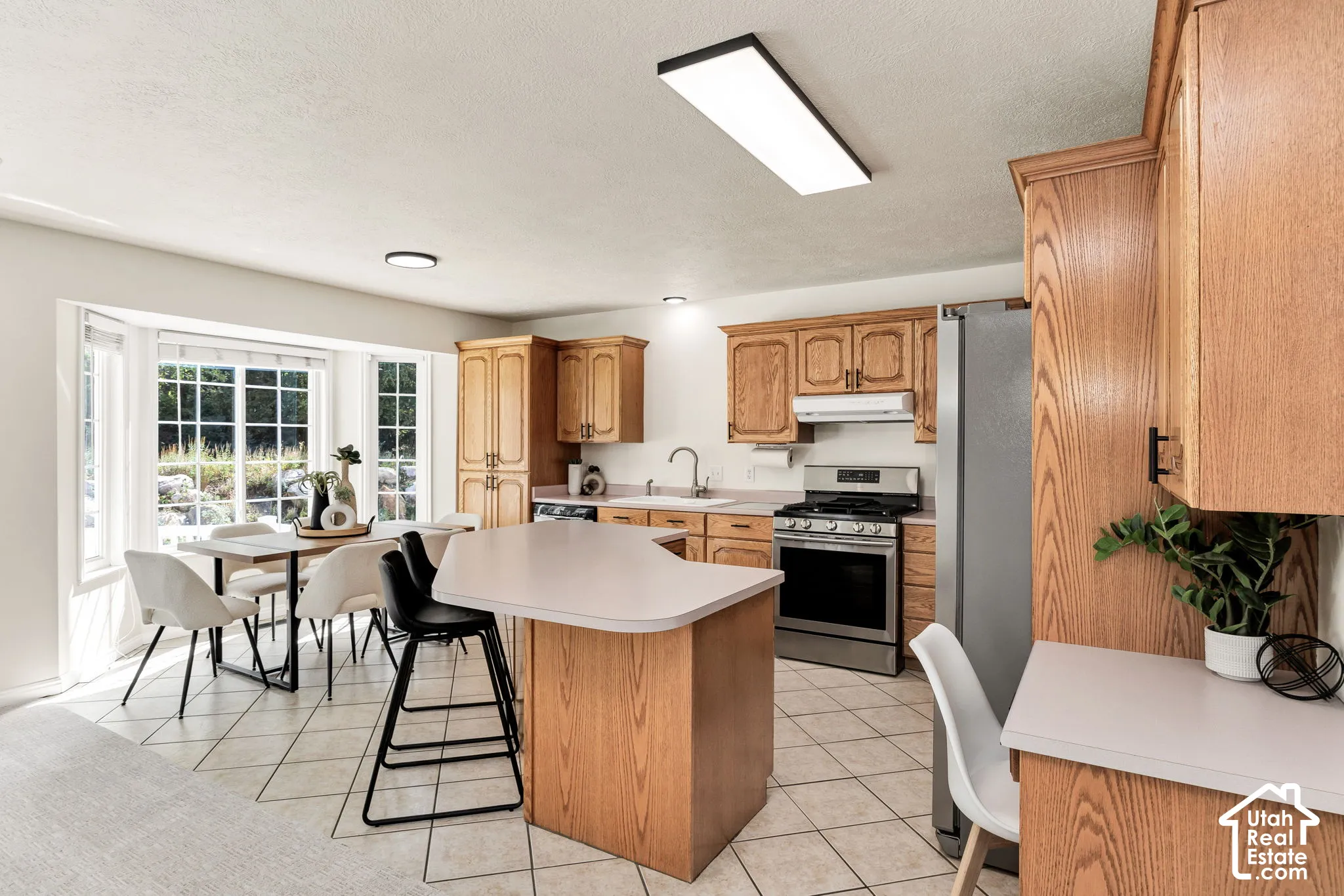 Kitchen featuring wood cabinetry, stainless steel appliances, a center island with countertop seating, tiled flooring, and a bay window