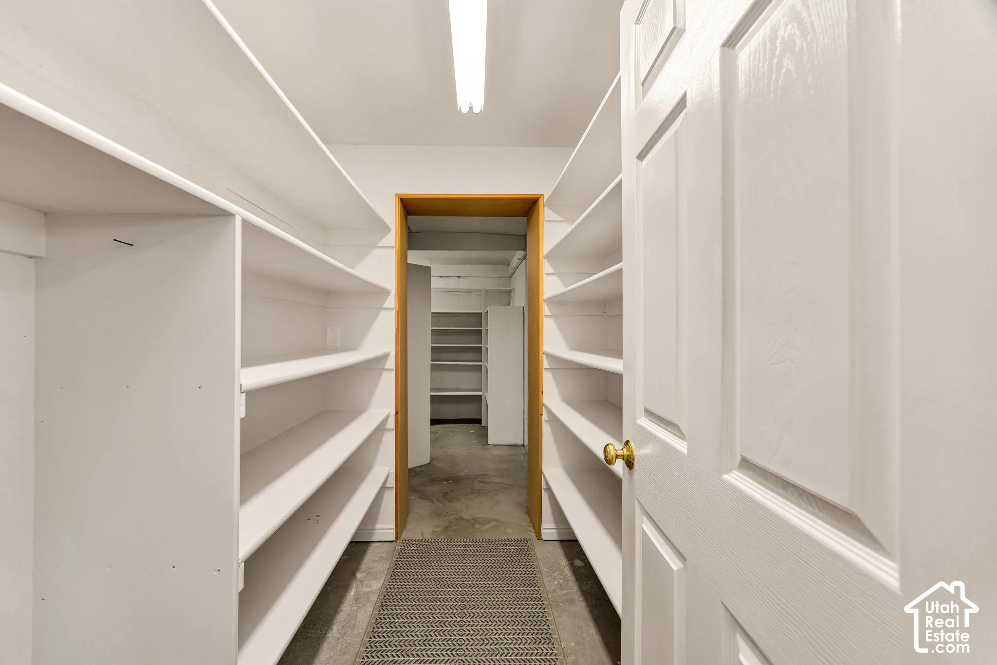 Extensive white shelving, concrete flooring, and a paneled white door with brass hardware