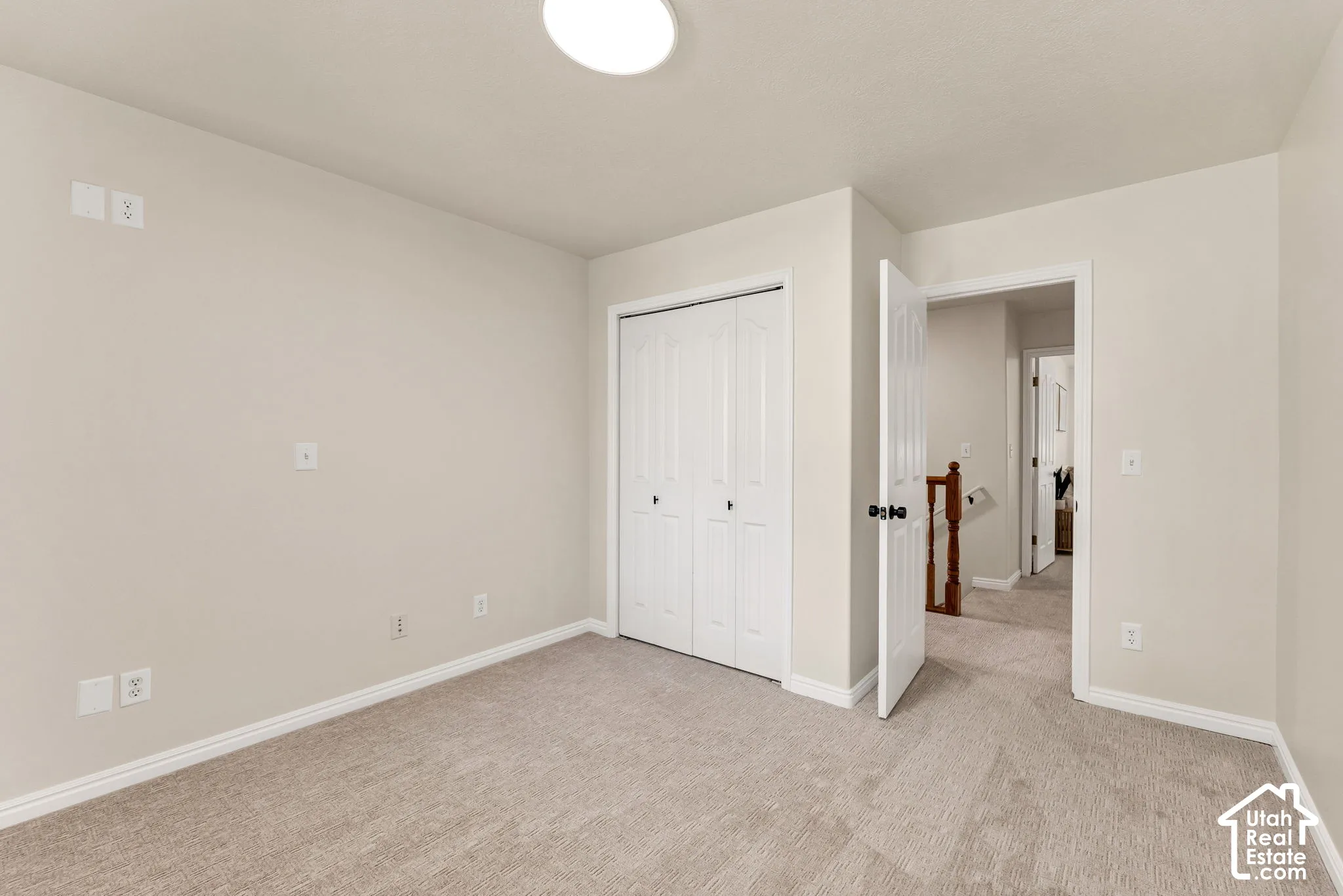 Neutral-toned carpet flooring, white bi-fold closet doors, white trim, and a white ceiling-mounted light fixture
