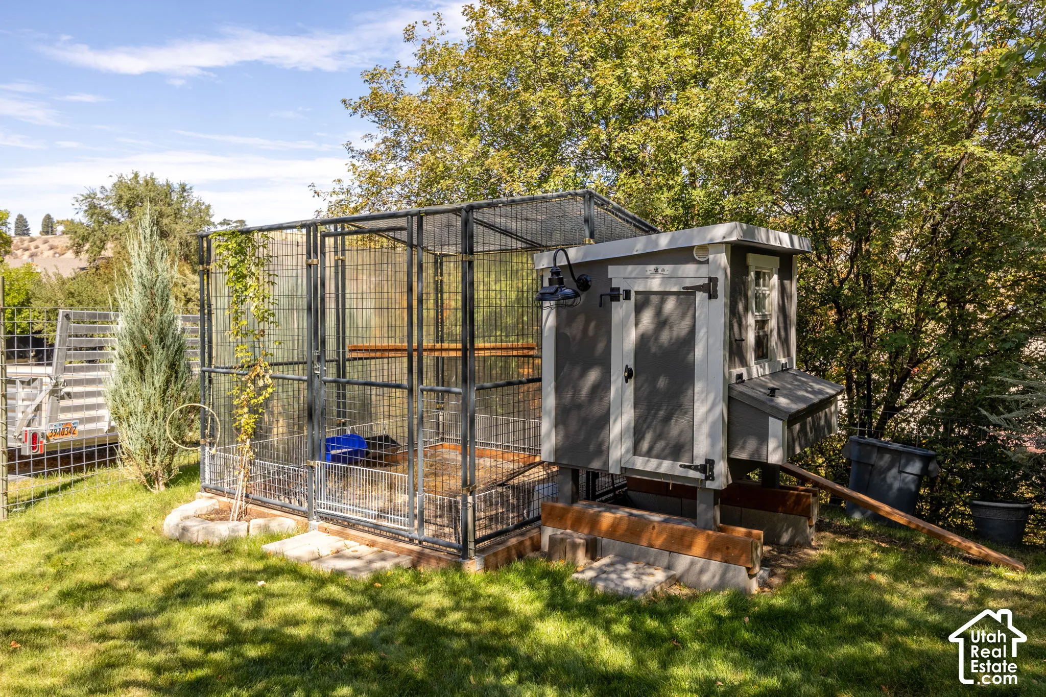 Well-maintained chicken coop with an attached wire enclosure, featuring a small window and exterior lighting fixture