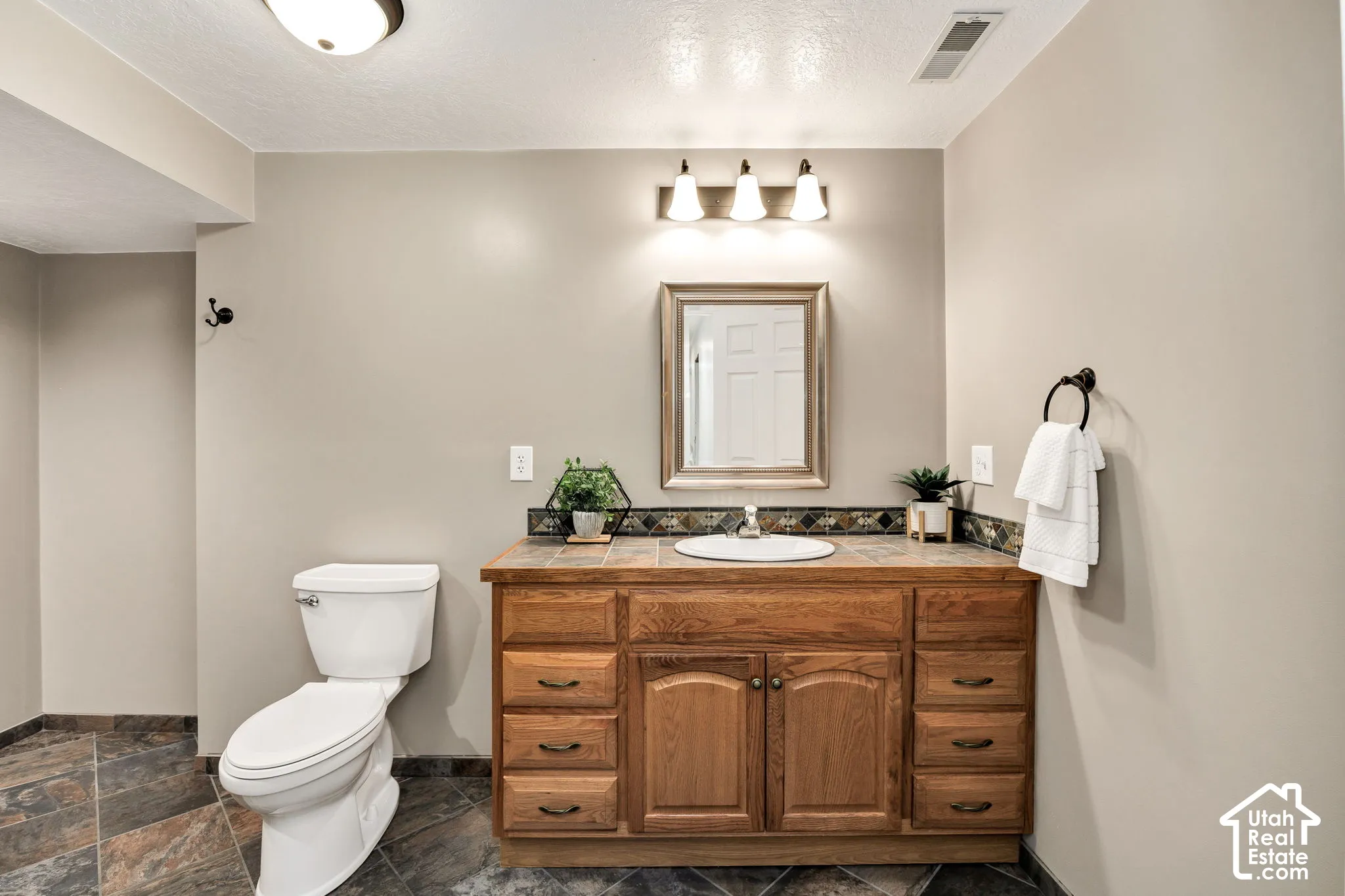 Wood-finish vanity with an integrated sink, tile countertop, and decorative tile backsplash