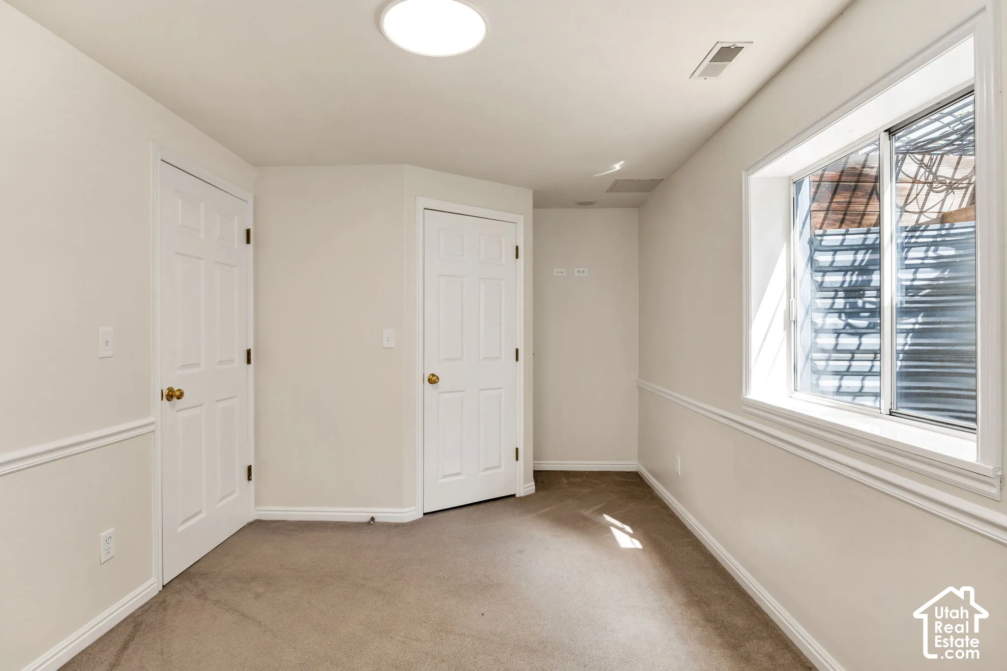 Recessed window with white trim, two white paneled doors, neutral carpeting, and a flush mount ceiling light