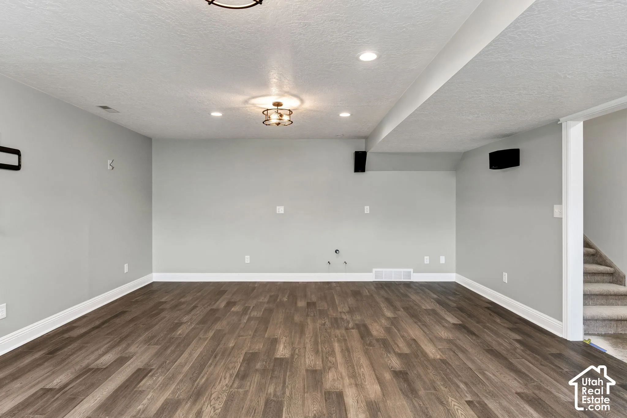 Spacious room featuring wood-finish flooring, light gray walls, recessed lighting, and a decorative ceiling fixture