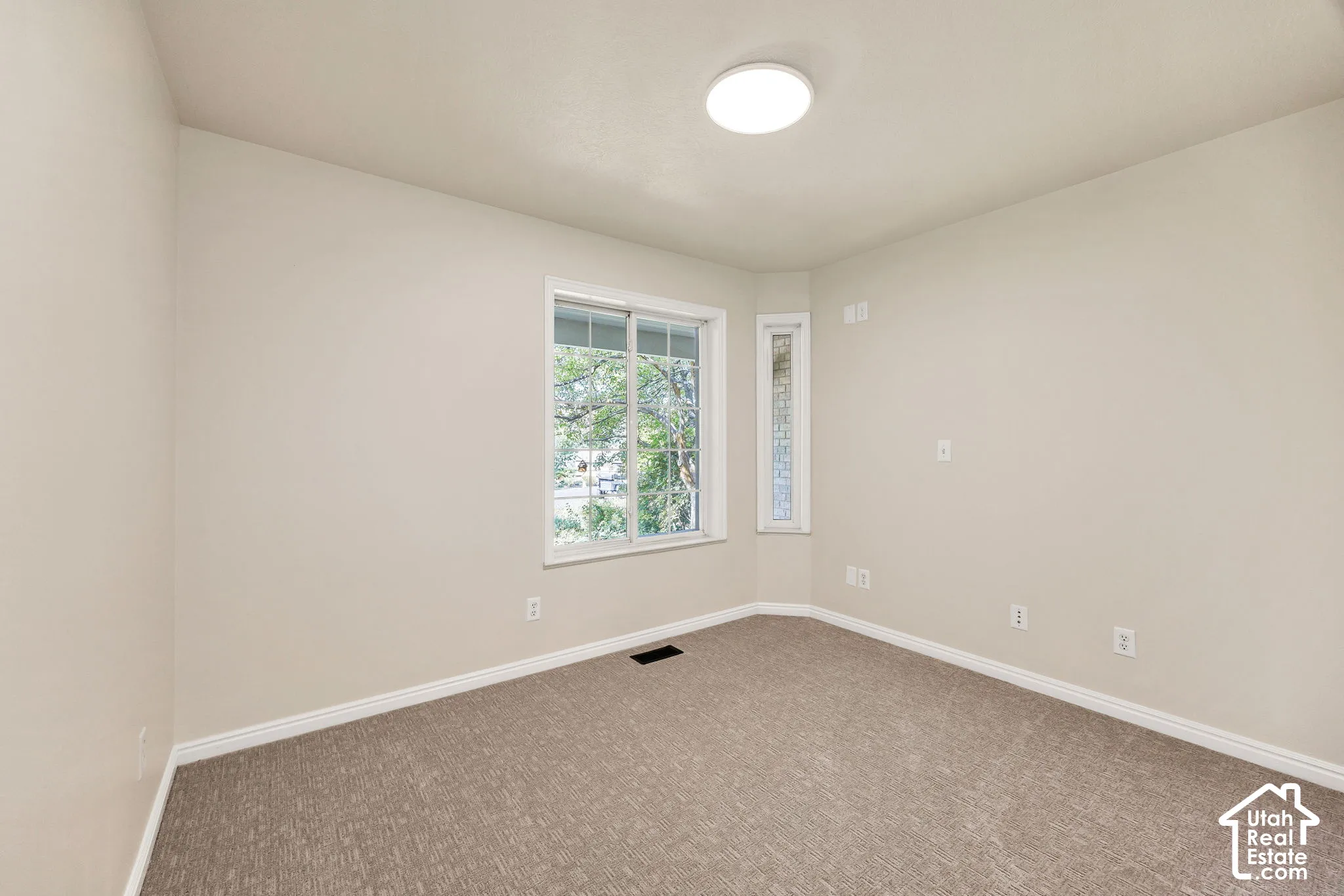 Neutral tone wall paint, textured carpeting, contemporary flush mount ceiling light, and window with natural light