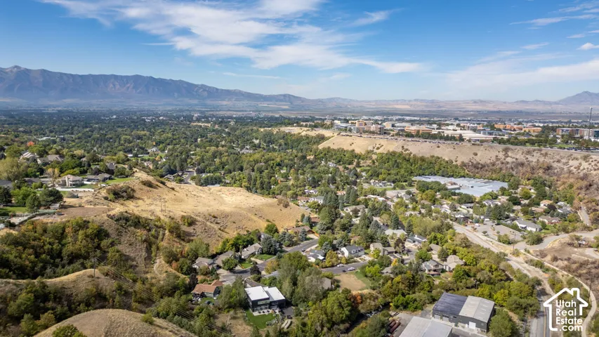 Expansive mountain range backdrop, established residential areas, abundant mature trees, varied topography with rolling hills, and distant commercial structures
