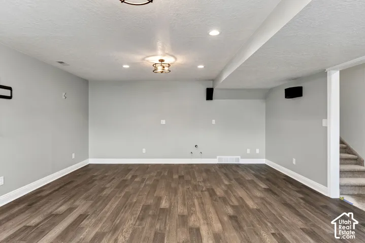Spacious room featuring wood-finish flooring, light gray walls, recessed lighting, and a decorative ceiling fixture