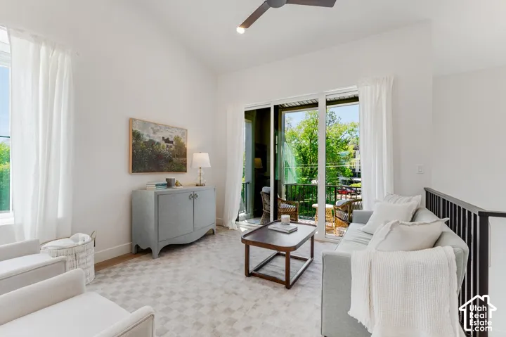 Vaulted ceiling with a ceiling fan, sliding glass door to a balcony, large window, and patterned carpet flooring