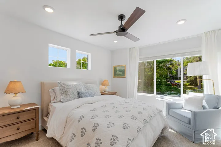 White walls with recessed lighting, ceiling fan with wood-finish blades, large window with sheer white curtains, and two smaller transom windows