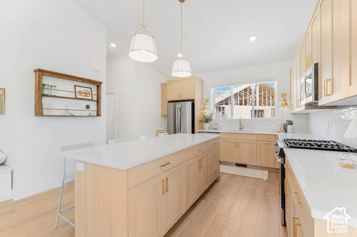 Spacious kitchen featuring an expansive center island with seating, light wood-finish cabinetry, white countertops, and wood-finish flooring