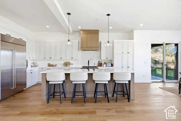 Open-concept kitchen featuring wood-finish flooring, white cabinetry, a large center island with seating, stainless steel appliances, and a light wood-finish range hood. The photos are renderings only - these photos are for a similar unit in Discovery Rid
