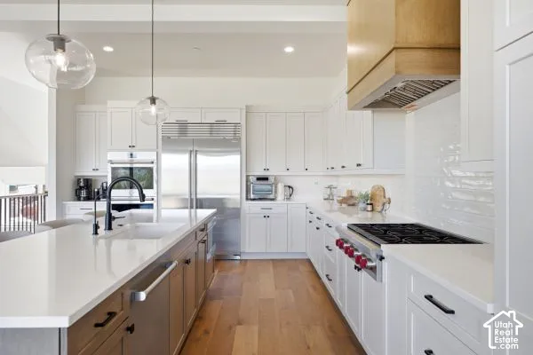Spacious kitchen featuring an expansive island, stainless steel appliances, wood-finish flooring, white cabinetry, and a subway tile backsplash. The photos are renderings only - these photos are for a similar unit in Discovery Ridge. Not this actual model