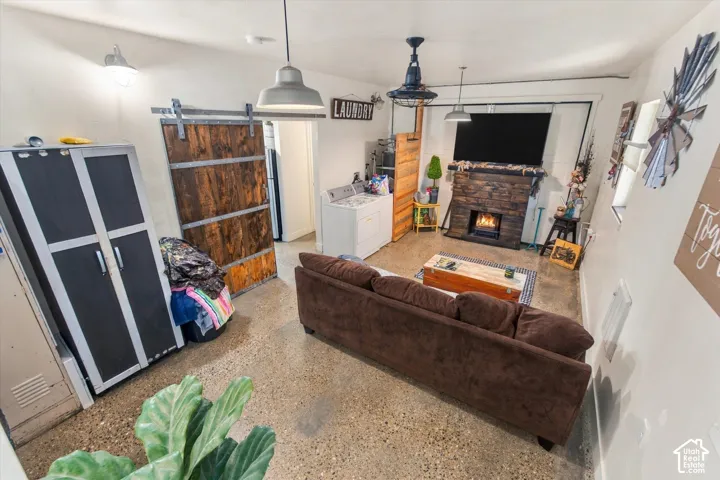 Exposed aggregate concrete flooring, stone-clad fireplace, wood barn door on a sliding track, and utility lighting fixtures