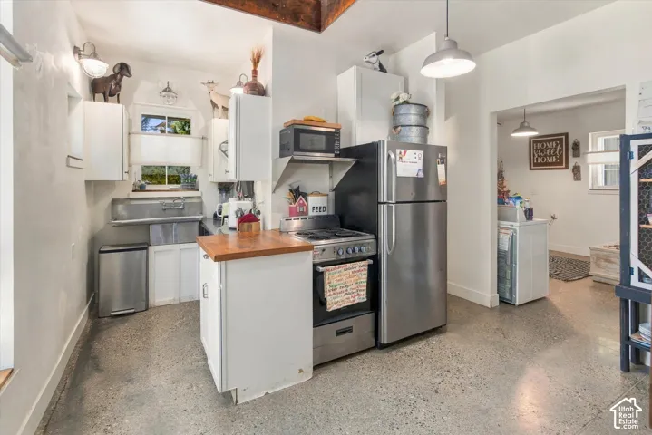 Exposed beam ceiling, concrete-finish flooring, white cabinetry, stainless steel appliances, and a wood-finish countertop