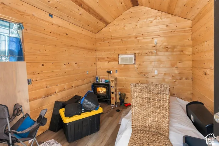 Wood-finish wall and ceiling paneling, pitched ceiling, window-mounted air conditioning unit, and a corner wood-burning stove