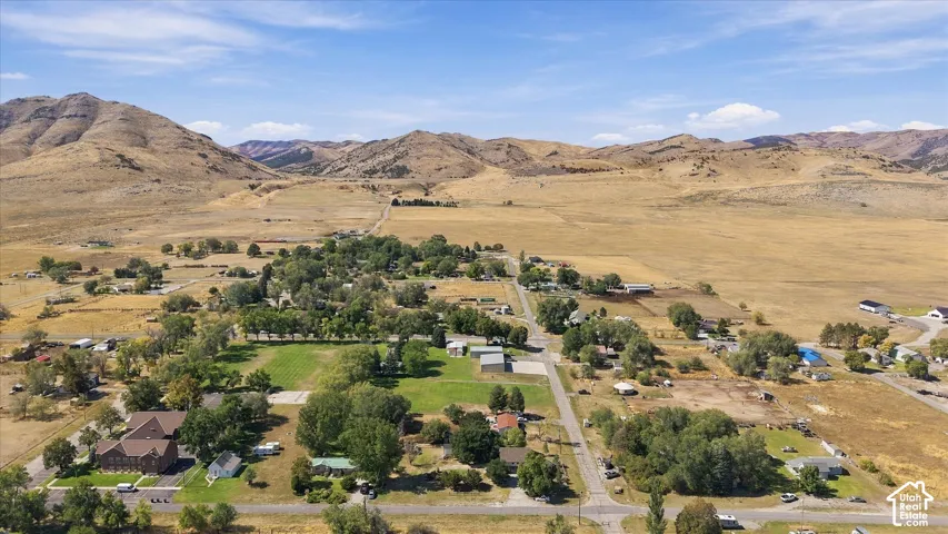 Expansive rural setting with mountainous terrain, scattered residential structures, and established trees