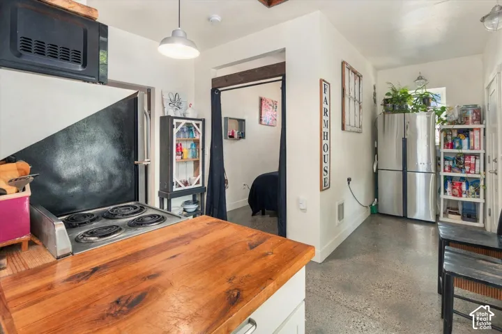 Wood-finish countertops, built-in electric cooktop, stainless steel refrigerator, and polished concrete flooring