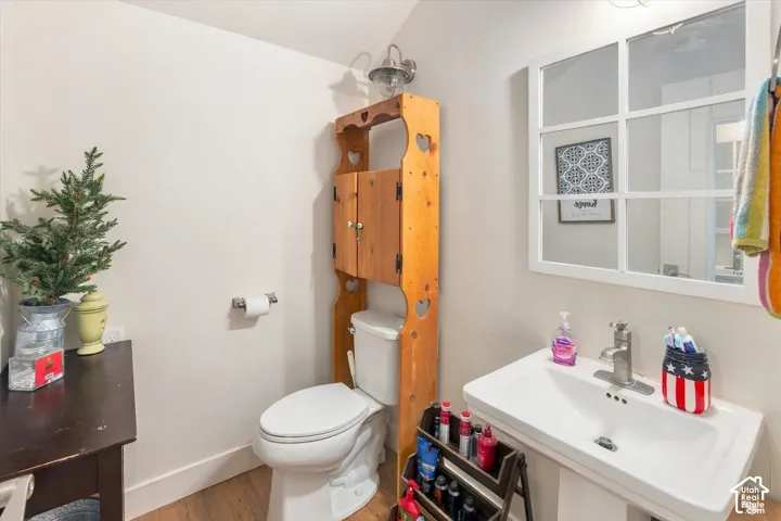 White pedestal sink with a single-handle faucet, window-pane style mirror, and wood-finish flooring