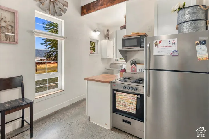 Kitchen featuring stainless steel appliances, wood-finish countertops, exposed wood beam, and concrete flooring