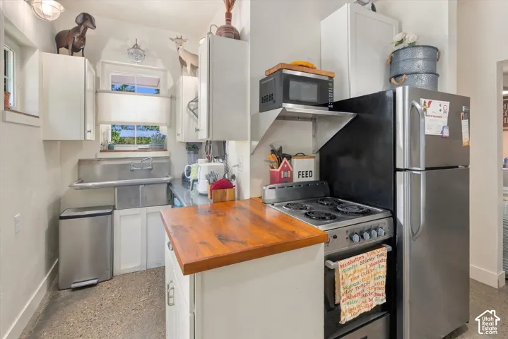 Compact kitchen featuring white cabinetry, stainless steel sink, wood-finish countertop, and a built-in range