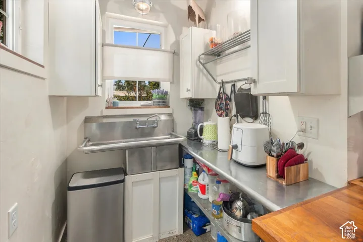 Stainless steel sink with a window above, white cabinetry, and stainless steel countertops